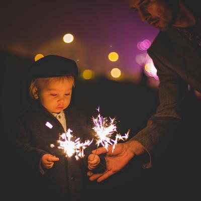 A father helping his young child with sparklers during a New Year celebration.