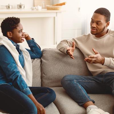 A couple sitting on the couch at home and having a serious conversation.