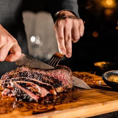 A butcher slicing a tomahawk steak in a serving table for a customer in a steakhouse restaurant.