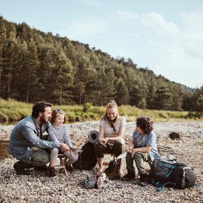 A family camping beside a small creek and cooking fish over a campfire.