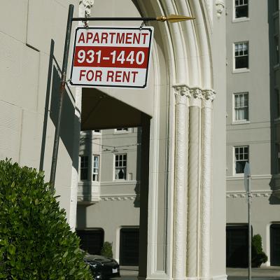An 'apartment for rent' sign hangs outside of an apartment building.