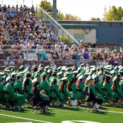  A high school graduation ceremony happening outdoors in the campus' sports field.