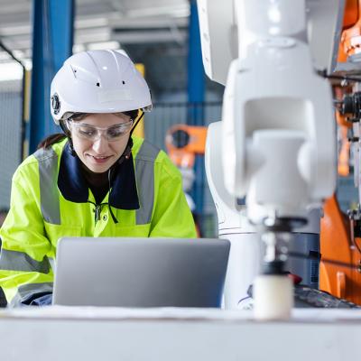 An engineer checking automation robotics from a laptop for a manufacturing machine in an industrial factory.