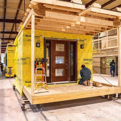 A worker kneels on a wooden platform building a modular home under construction in a factory in Middleburg, Pennsylvania.