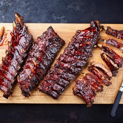 Slabs of freshly barbecued ribs sliced on a wooden cutting board.
