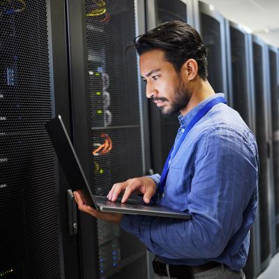 A programmer working on a laptop for maintenance and network server checking in a data center.