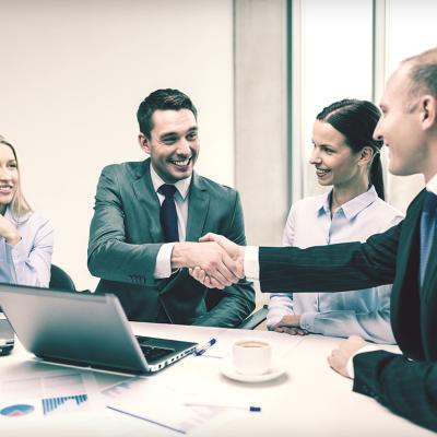 A business team with its two leaders shaking hands during a meeting.