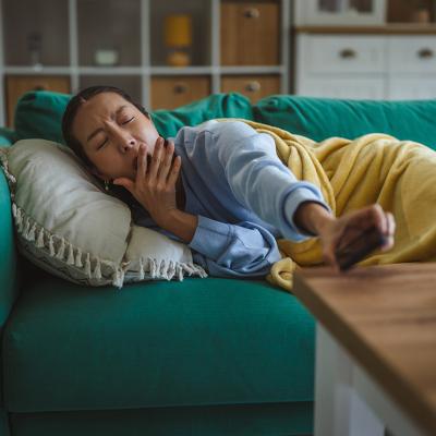 A young woman at home yawning and lying comfortably on a green couch.
