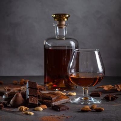 A glass of cognac, cognac in a bottle and pieces of chocolate on a dark background.