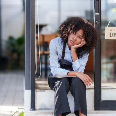A female shopkeeper stressfully sat outside her store.