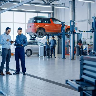 A manager explaining diagnostics results and vehicle breakdown to a mechanic in a car workshop.