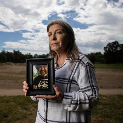 Jeanelle Couch holds framed photo of her son, David Couch, who was killed in a shooting involving a California Highway Patrol officer. She is standing in Cascade Park in Redding with a sky full of clouds and open space behind her.