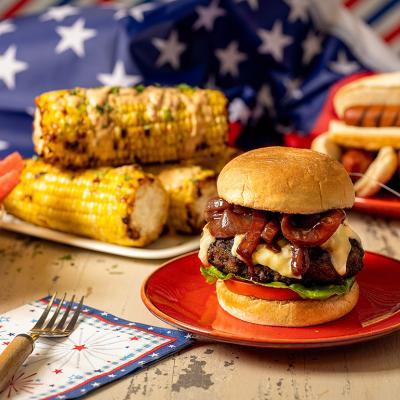 Plates of hamburger, corn, and hotdogs for Fourth of July festivities.
