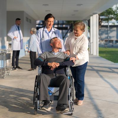 A female doctor assisting her patient in pushing his wheelchair along with a companion.