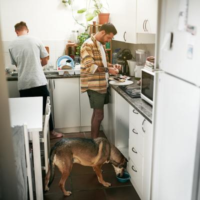 A young gay couple cooking together in their kitchen and feeding their dog.