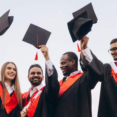 A group of graduates celebrate by holding their graduation caps in the air.