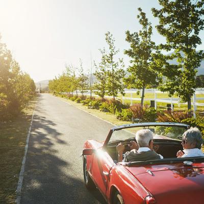 An elderly couple driving in a convertible car for a road trip on a summer day.