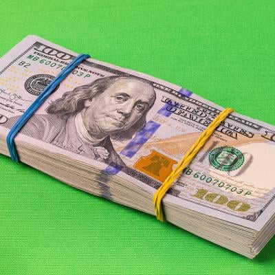 A pack of 10,000 U.S. dollars laid on a striking green background.