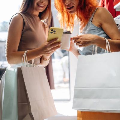 Two friends checking items' information from a smartphone after shopping clothes in a store.