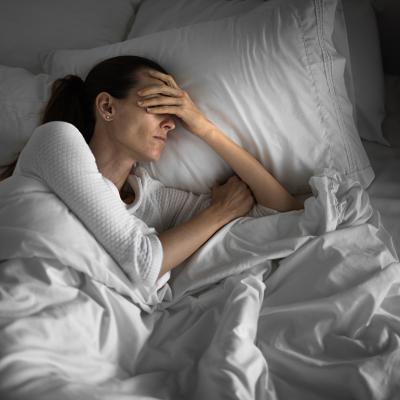 A tired woman in bed struggling to sleep.