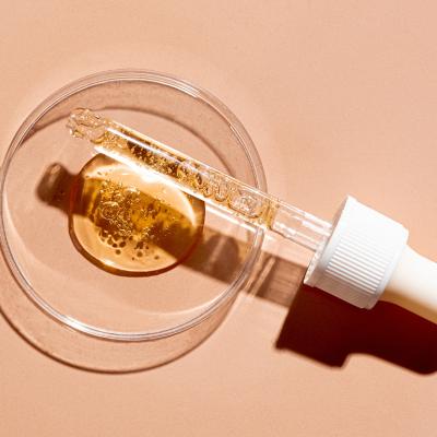 A dropper pipette and a petri dish with drops of oil or retinol gel on a beige nude background.