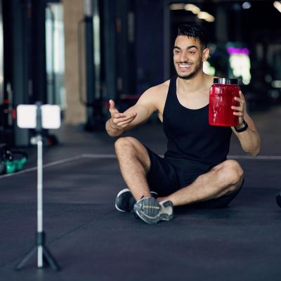 A fitness blogger recording himself from his smartphone at a gym for a sport wellness video.