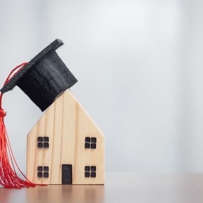 A miniature figures of a graduation cap on a wooden house, symbolizing the concept of success in education.