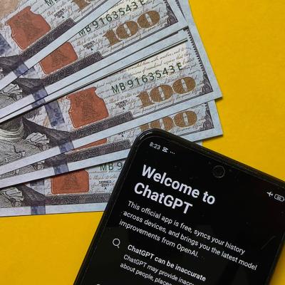 US 100 dollar banknotes and a smartphone displaying ChatGPT in a yellow background, symbolizing the concept of financial AI.