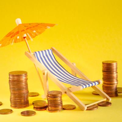 Coins around a beach deck chair and umbrella as a concept of saving for a holiday.