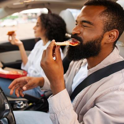 A couple eating pizza in the car during a road trip.
