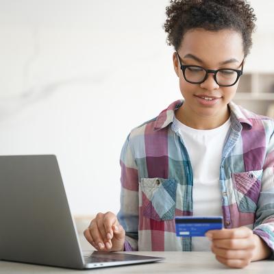 A teenager holding a credit card while shopping online from a laptop.