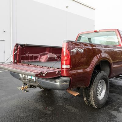 A burgundy 2000 Ford F-250 Super Duty pickup truck parked in an outdoor garage with its tailgate open.