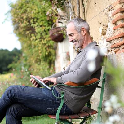 A middle-aged man using phone while sitting on a bench in a countryside home.