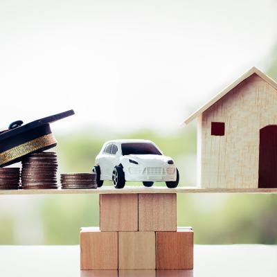 Miniatures of a graduation cap on top of coin stacks, a car, and a house above a wooden block, symbolizing the concept of success in university education.