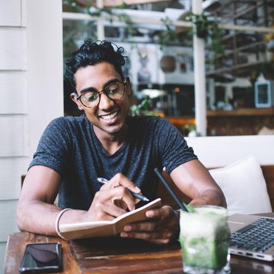 A happy young man taking notes while studying at a cafe.