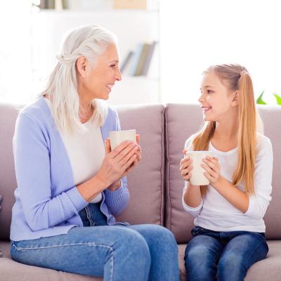 A mother and her young daughter enjoying a hot drink on the sofa.
