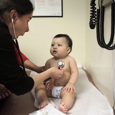 A pediatrician distracts a 9-month-old boy to check his heartbeat.