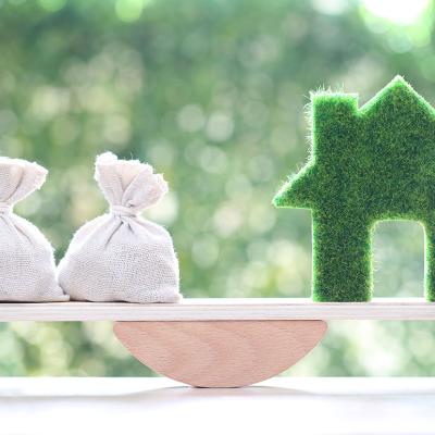 A bag of money and a figure of a home on both ends of a seesaw as a concept of weighing finances and home equity.