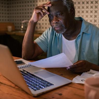 An elderly man reviewing his budget and finances from a laptop at home.