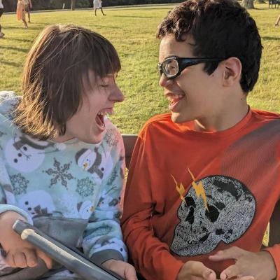 Two young individuals with disabilities happily engaging in a conversation outdoors.