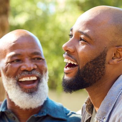A senior father with his adult son happily engaged in a conversation outdoors.