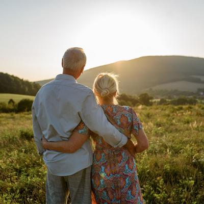 An elderly married couple enjoying the sunset view after a walk.