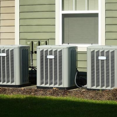 Three air conditioner compressor units placed behind a house.
