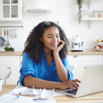 A young woman paying bills online in her home kitchen.