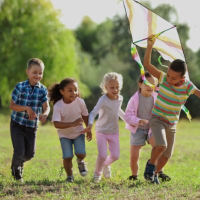 A group of happy kids running in a park. One boy is holding a kite. 