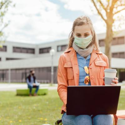 A woman wearing a mask while on a computer.