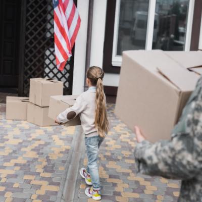 A man in camo and a young girl moving boxes into a house.