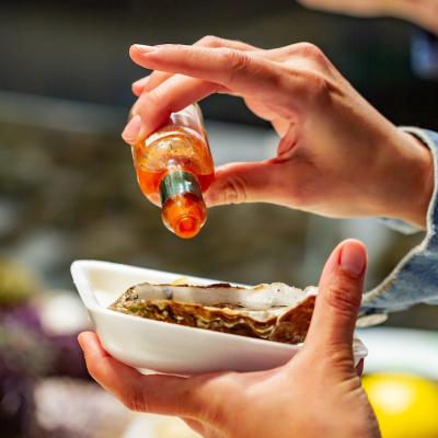 Pouring hot sauce over oyster on white plate.