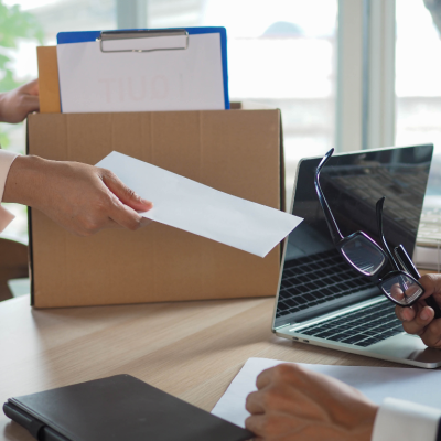 Person puts box of personal belongings on desk and hands boss resignation letter.