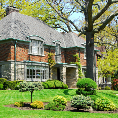 A large two-story brick and stone house with a well-manicured front lawn in an affluent neighborhood.